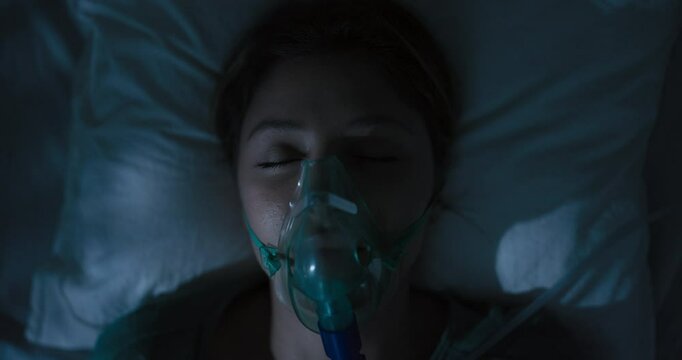 Sad tired woman in oxygen mask coughing heavily breathes.
