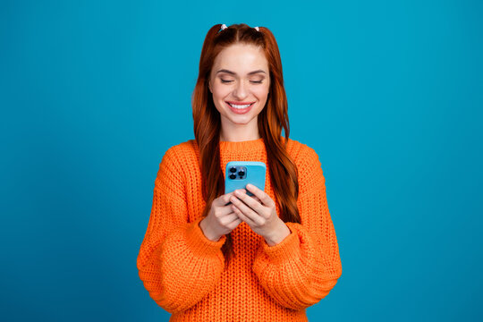 Photo of charming positive girl wear orange sweater chatting apple iphone samsung modern device empty space isolated blue color background - Powered by Adobe