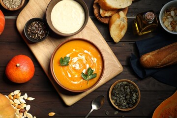 Delicious pumpkin soup with sour cream, spices and products on wooden table, flat lay