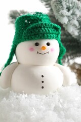 Cute decorative snowman and fir tree branches on artificial snow against white background, closeup