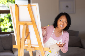 asian senior woman painting on canvas at home, smiling and enjoying creativity