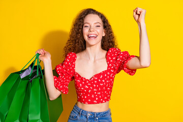 Photo portrait of lovely young lady shopping bags winning dressed stylish red garment isolated on yellow color background