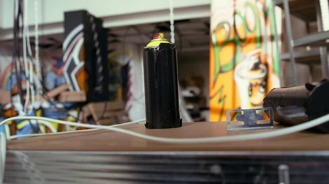 Close up of spray cans in empty basement with graffiti drawings on walls. Focus on paint cans with underground warehouse used as crime haven by hooligans in blurry background
