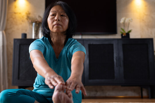 Asian senior woman practicing yoga at home, stretching and focusing on flexibility