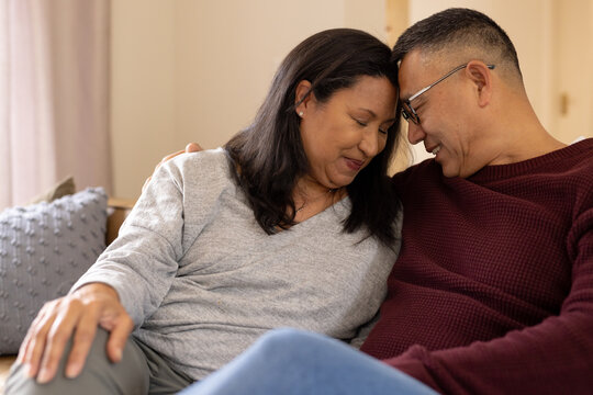 Multiracial senior couple sharing tender moment at home, embracing and smiling warmly
