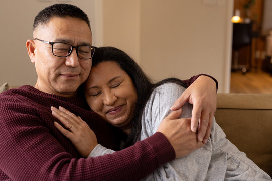 Senior multiracial couple embracing on cozy sofa, sharing warm holiday moments at home