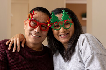 Smiling Senior multiracial couple wearing festive glasses, celebrating Christmas at home