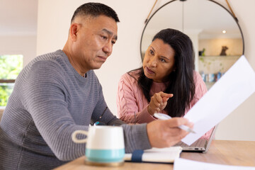 Multiracial senior couple discussing finances at home, reviewing documents together seriously