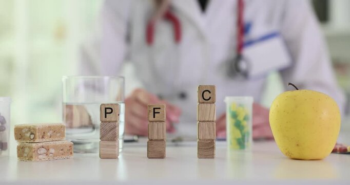 Letters PFC on wooden cubes columns as graph against doctor working at desk. Protein fats and carbohydrates balance in everyday nutrition