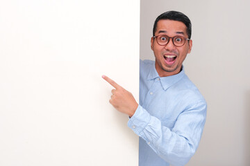 A man peeking behind wall showing wow face while pointing at the wall