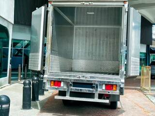 A cargo truck with its rear doors open, showcasing a clean metal interior, parked in an urban outdoor setting