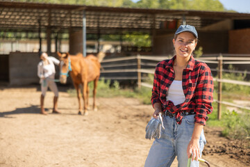Young woman poses while cleaning horse paddock