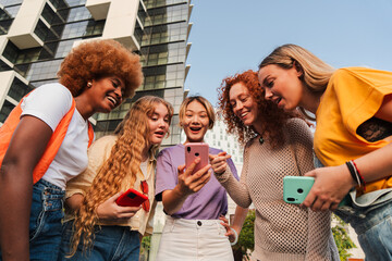 Diverse group of young women excitedly using a smartphone outdoors. Friends browsing the internet...