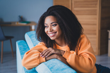 Photo of lovely young girl sit couch look dreamy empty space dressed orange garment spend pastime...