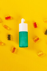 Cosmetic product in tube, bottle, lotion or serum and colorful candies, jelly on yellow background. 