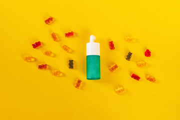 Cosmetic product in tube, bottle, lotion or serum and colorful candies, jelly on yellow background. 
