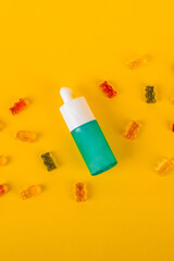 Cosmetic product in tube, bottle, lotion or serum and colorful candies, jelly on yellow background. 