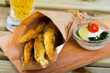 Delicious popular beer snack - pan-fried anchovies (fish chips) served in paper cone with creamy...