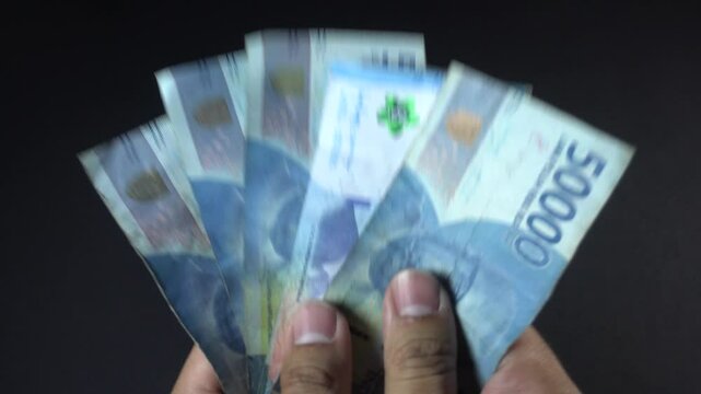 A man's hand holding and counting on some fifty thousand rupiahs indonesian currency on solid black background