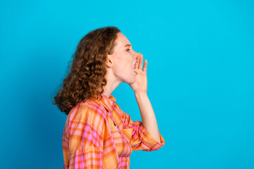 Vibrant young woman with curly hair shouting enthusiastically against a bright blue background