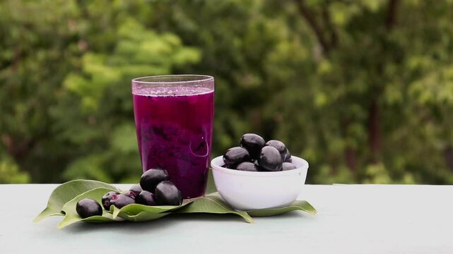 Jamun or Malabar Plum Juice in a Glass with Fruit in a Bowl with Leaves Isolated on Wooden  Background, Also Known as Black Plum, Syzygium Cumini or Jambolan