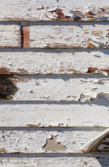 Close-up of peeling white paint on aged wooden siding with weathered texture and cracks.