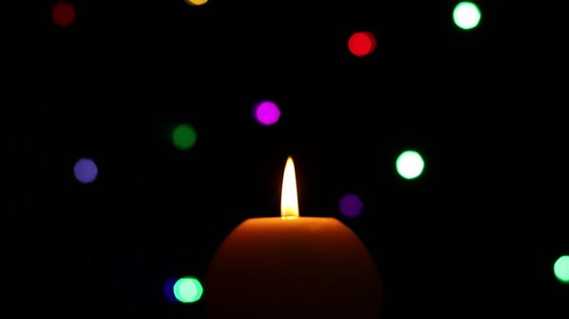 Una toma de cerca de una vela con llama de color blanca rodeada de luces de navidad de varios colores.  Decoraci&oacute;n de navidad y fin de a&ntilde;o