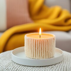 Cozy candle with flame on a plate, soft blanket in the background.