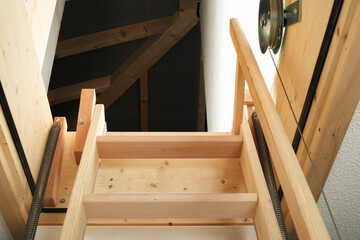 Open attic door with ladder. Expandable loft sliding ladder to access attic space or loft. Spring coil and wire pulley. Space saving storage space. Selective focus. Lucerne, Switzerland.