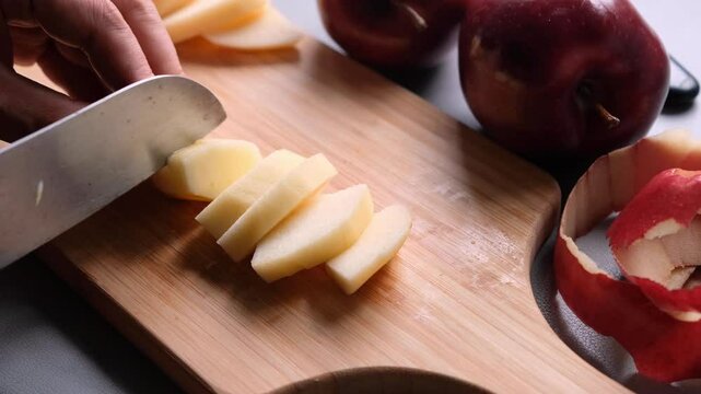 Close up of man's hands cutting red apple on the cutting board in the kitchen.
