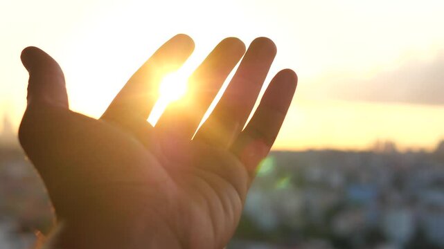 A Hand Extending Gracefully Towards the Bright Sunlight Shining Above the Urban Cityscape Below