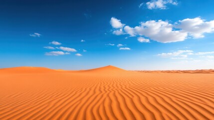 Expansive desert landscape under a clear blue sky with gentle cloud formations and wind-swept sand dunes.