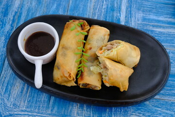 vegetable fried spring rolls in a black plate on a blue table. soy sauce near the spring rolls. lumpia. 