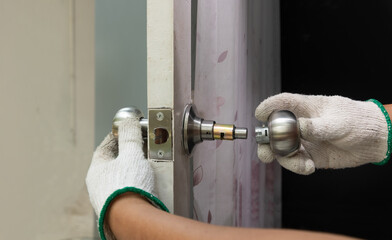 Locksmith on wood door with screwdriver for repair or fix silver knob.