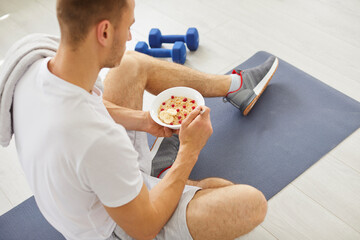 Man enjoying a healthy food, oatmeal with fruits at home during a break from workout. The...