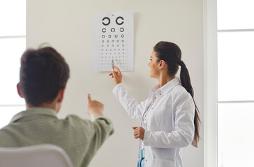 Doctor ophthalmologist or optometrist, conducts a vision checkup for a patient using a vision chart in a clinic. Healthcare professional provides ophthalmology care to ensure the patient eye health.