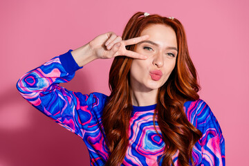 Photo portrait of lovely young lady show v-sign kissing lips dressed stylish blue colorful garment isolated on pink color background