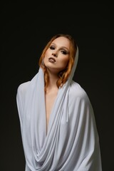 Woman draped in elegant white fabric poses against a dark background