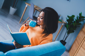 Photo of attractive young woman sit couch drink tea read book dressed orange outfit cozy day light...