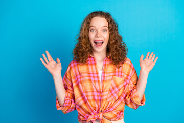 Excited young woman gesturing surprise in colorful plaid shirt on bright blue background