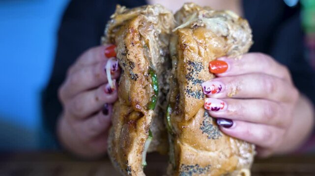 Extreme closeup of a classic NYC bodega style Chopped Cheese Sandwich with pickles being opened in half in slow motion by hands with a perfect manicure to reveal the fillings