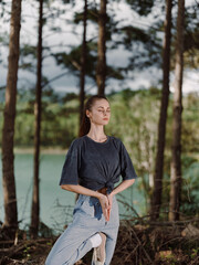 Obraz premium Serene young woman practicing yoga in a tranquil forest setting, surrounded by tall trees and a calm lake Wellness and mindfulness concept emphasizing nature