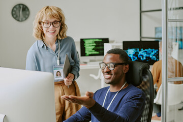 Ethnically diverse cheerful young man and woman working in modern IT company looking at screen and...