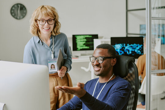 Ethnically diverse cheerful young man and woman working in modern IT company looking at screen and discussing new project