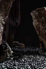 Set in a minimalist setting with huge rough rocks and charcoal samples, surrounding a pebbled...