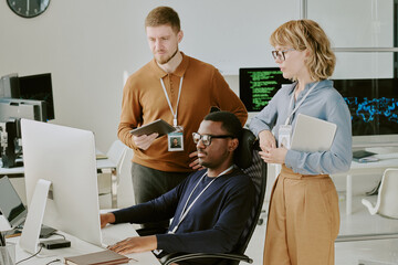 Group of three young ethnically diverse IT specialists working together on cybersecurity software...