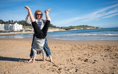 Mother and son playing and pirouetting on a beautiful day at the beach during a winter vacation