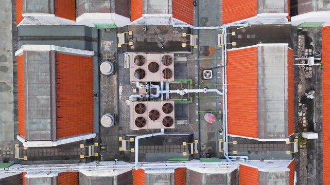 Drone top down rises above AC vent and fan units on top of orange tiled rooftop, industrial texture centered over building complex