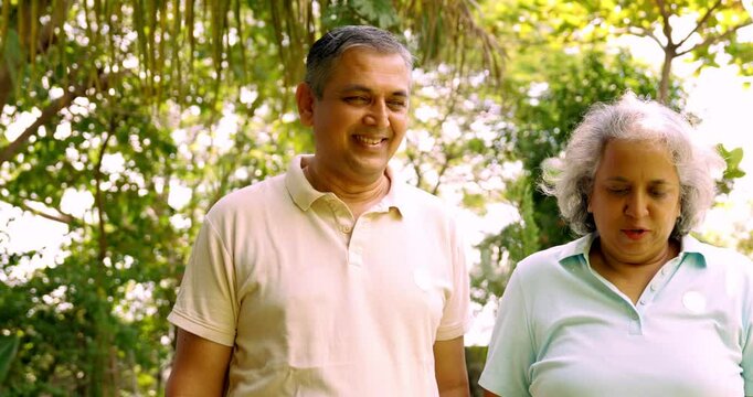 Indian Asian mid age couple in their fifties walking in the park, smiling and pointing, enjoying a pleasant conversation on a sunny day outdoors