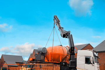 A construction truck delivers a concrete mixer to a construction site under a bright blue sky